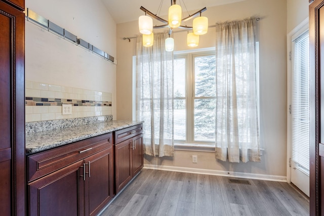 kitchen with decorative light fixtures, light wood-type flooring, plenty of natural light, light stone countertops, and decorative backsplash