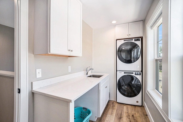 clothes washing area with sink, light hardwood / wood-style flooring, stacked washer / dryer, and cabinets