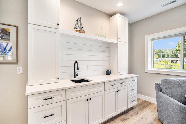 interior space featuring sink, white cabinetry, light hardwood / wood-style flooring, and light stone counters