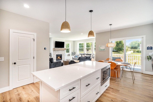 kitchen featuring stainless steel microwave, white cabinetry, hanging light fixtures, and light hardwood / wood-style floors