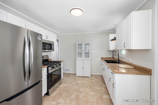 kitchen featuring appliances with stainless steel finishes, sink, white cabinets, crown molding, and light stone countertops