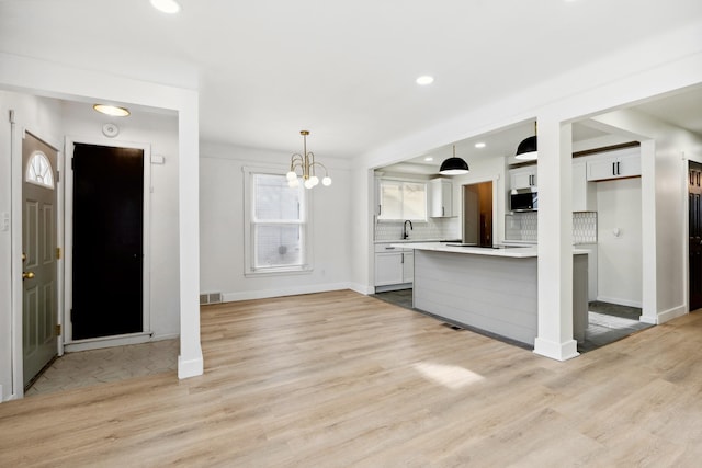 kitchen with pendant lighting, sink, light wood-type flooring, white cabinetry, and tasteful backsplash