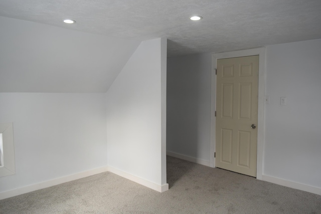 additional living space with lofted ceiling, light carpet, and a textured ceiling