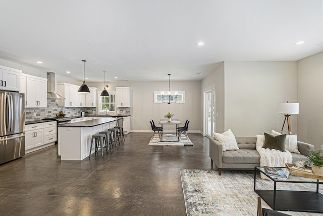 kitchen with pendant lighting, wall chimney range hood, a breakfast bar, appliances with stainless steel finishes, and a center island