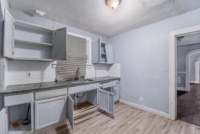 kitchen with tasteful backsplash, gray cabinets, sink, and light wood-type flooring