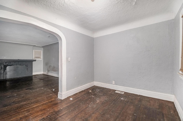 spare room featuring dark wood-type flooring, a fireplace, and a textured ceiling