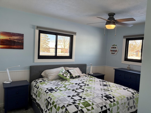 bedroom featuring a wainscoted wall, a textured ceiling, and a ceiling fan