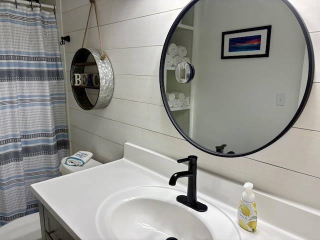 bathroom with curtained shower, wood walls, vanity, and toilet