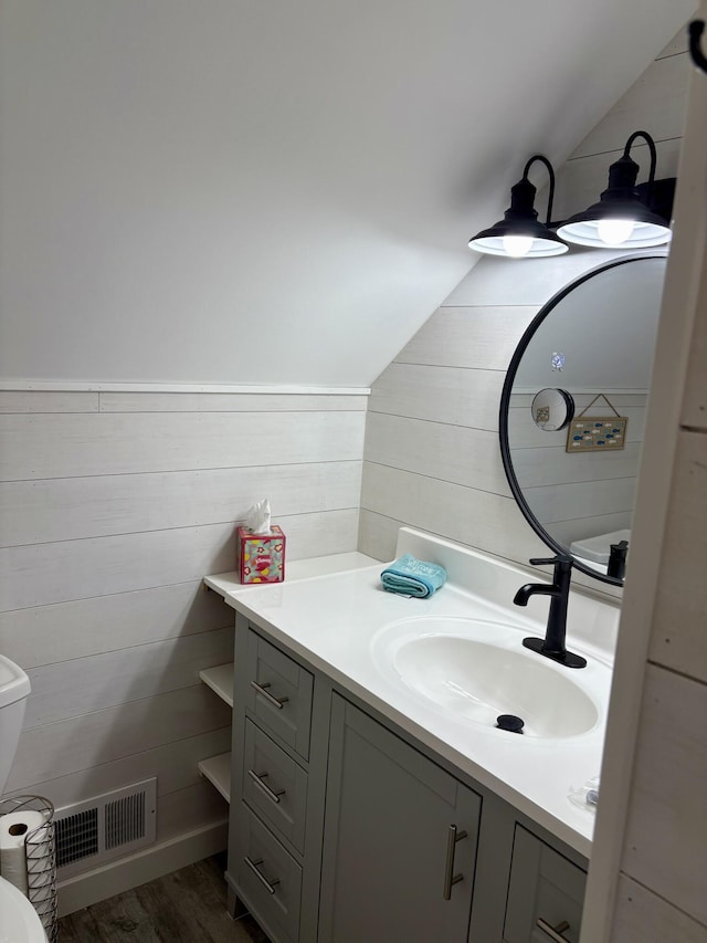 bathroom featuring wooden walls, visible vents, vaulted ceiling, and vanity