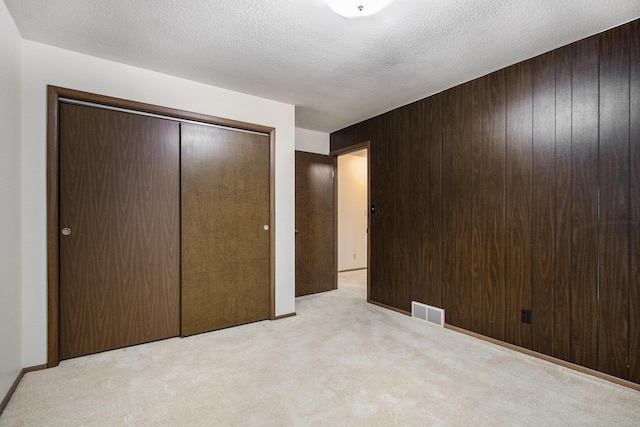 unfurnished bedroom featuring a textured ceiling, light carpet, a closet, and wood walls