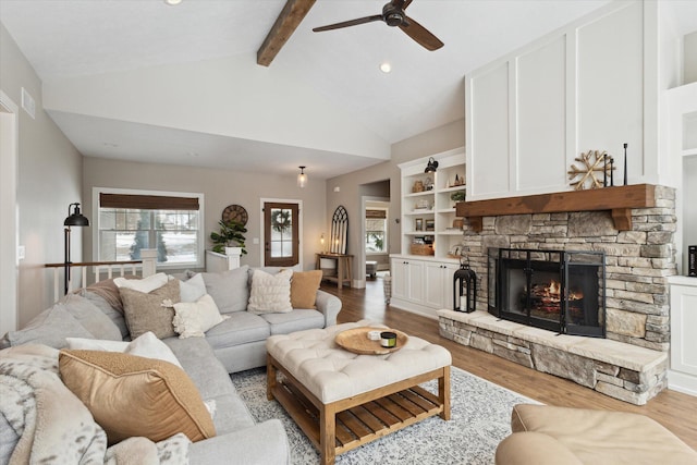 living room featuring built in shelves, light hardwood / wood-style flooring, lofted ceiling with beams, and a stone fireplace