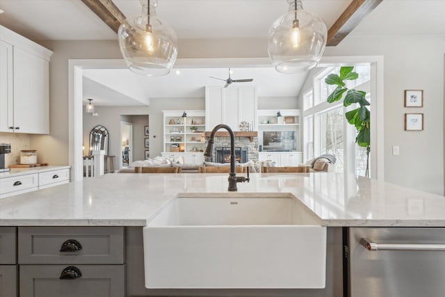 kitchen with sink, white cabinets, backsplash, light stone counters, and a center island with sink