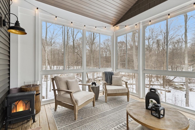 sunroom with wood ceiling, vaulted ceiling, a wealth of natural light, and a wood stove