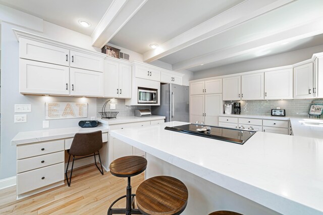 kitchen with white cabinetry, beamed ceiling, stainless steel appliances, and a breakfast bar area