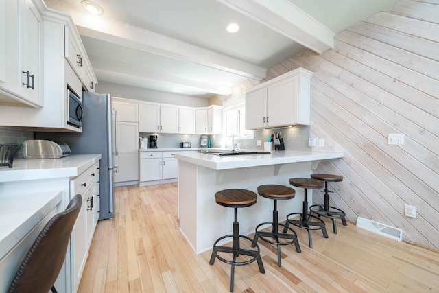 kitchen with a breakfast bar area, white cabinetry, beam ceiling, and stainless steel microwave