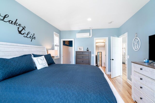 bedroom featuring a walk in closet, a wall mounted air conditioner, and light wood-type flooring