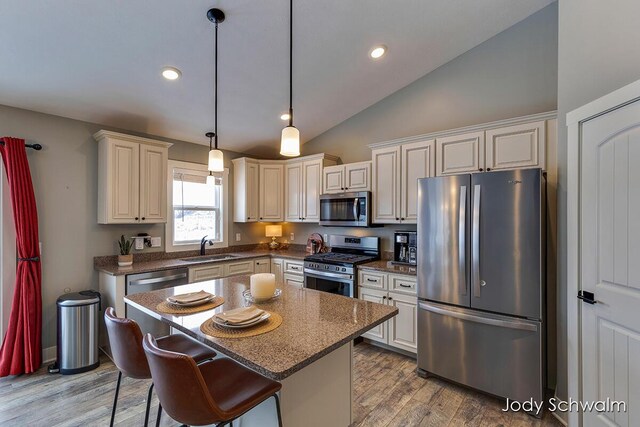 kitchen featuring sink, appliances with stainless steel finishes, light hardwood / wood-style floors, a kitchen island, and decorative light fixtures