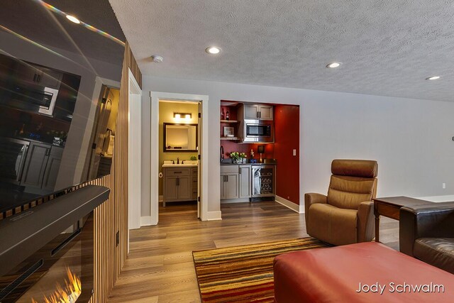 living room with wine cooler, light hardwood / wood-style flooring, a textured ceiling, and indoor bar