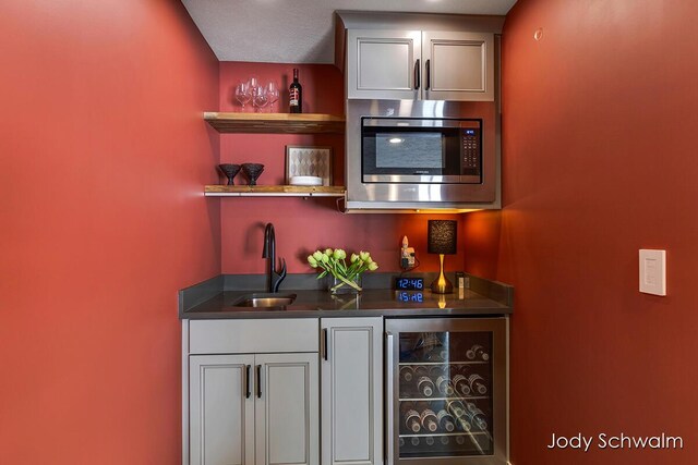 bar with stainless steel microwave, beverage cooler, and sink