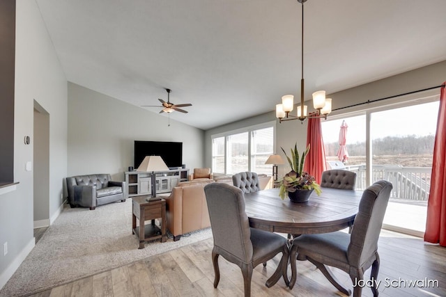 dining room featuring baseboards, ceiling fan with notable chandelier, light wood-style flooring, and vaulted ceiling