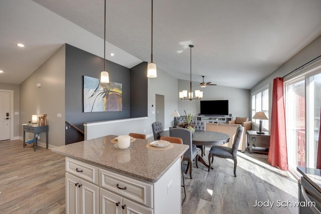 kitchen with light wood finished floors, open floor plan, pendant lighting, lofted ceiling, and light stone counters