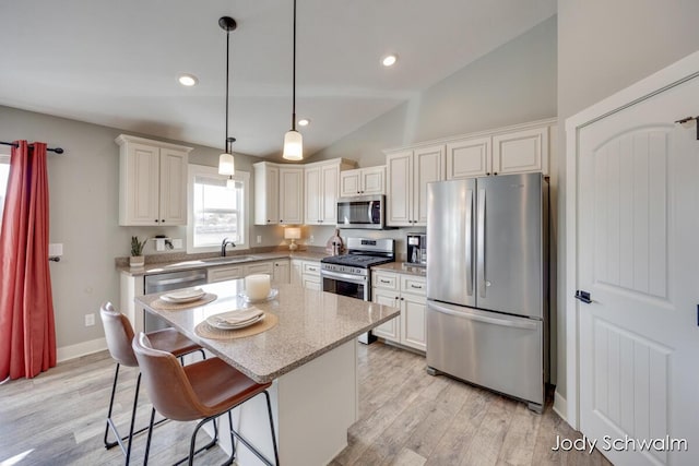 kitchen featuring lofted ceiling, a sink, stainless steel appliances, decorative light fixtures, and light wood-type flooring