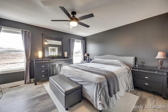 bedroom with a ceiling fan, wood finished floors, visible vents, and baseboards