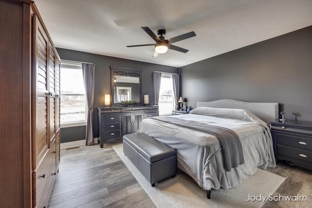 bedroom featuring light wood finished floors, multiple windows, baseboards, and a ceiling fan