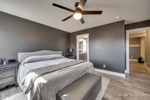 bedroom featuring ensuite bathroom, a ceiling fan, a sink, wood finished floors, and baseboards