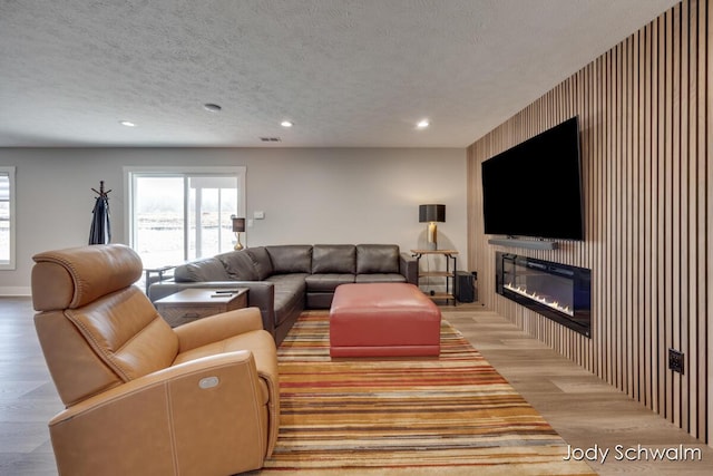 living area featuring light wood-type flooring, visible vents, a textured ceiling, a glass covered fireplace, and recessed lighting