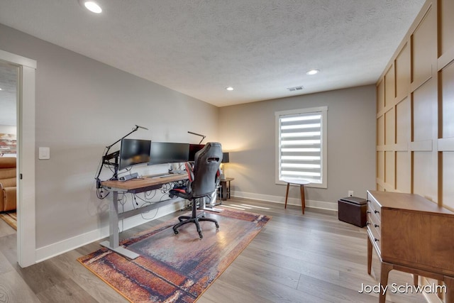 office featuring visible vents, light wood-style floors, baseboards, and a textured ceiling