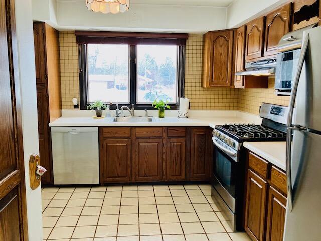 kitchen featuring sink, extractor fan, light tile patterned floors, stainless steel appliances, and backsplash