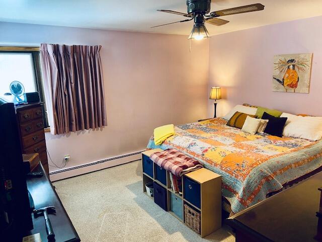 carpeted bedroom with ceiling fan and a baseboard heating unit