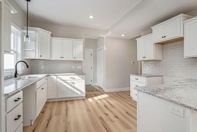 kitchen with sink, backsplash, white cabinets, hanging light fixtures, and light hardwood / wood-style floors