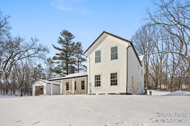 snow covered back of property featuring a garage, an outdoor structure, and a porch