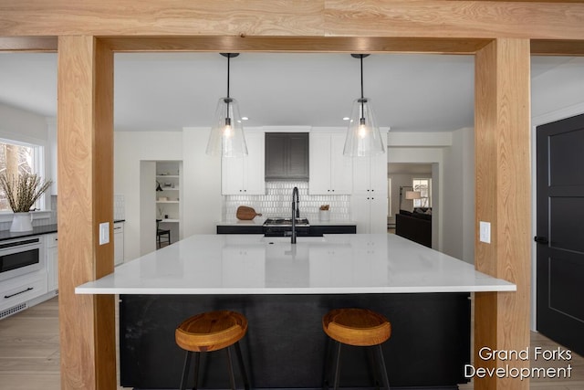 kitchen featuring a kitchen island with sink, decorative backsplash, and decorative light fixtures