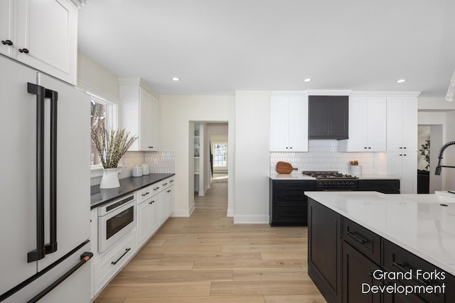 kitchen featuring built in microwave, high end white refrigerator, stovetop, decorative backsplash, and light hardwood / wood-style flooring