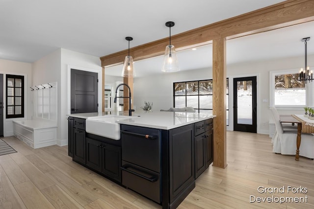 kitchen with decorative light fixtures, an island with sink, sink, a notable chandelier, and light wood-type flooring