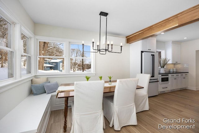 dining room with breakfast area, an inviting chandelier, light hardwood / wood-style floors, and beamed ceiling