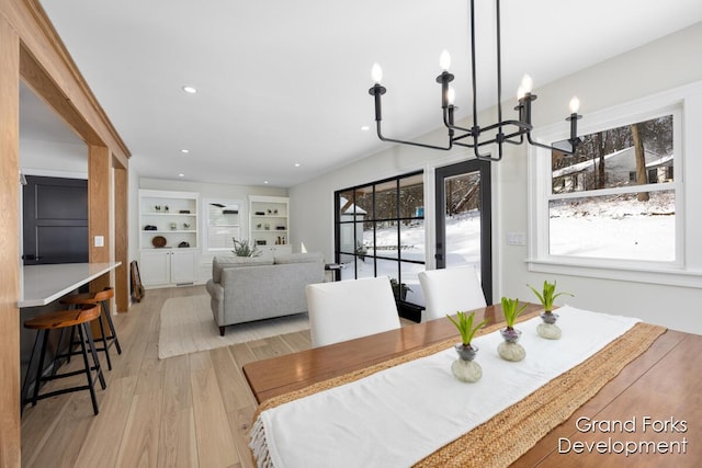 dining area with light hardwood / wood-style flooring, a notable chandelier, and built in shelves