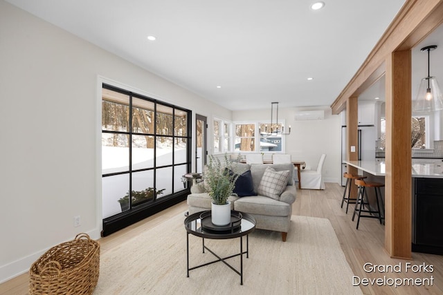 living room featuring an inviting chandelier, a wall mounted air conditioner, and light hardwood / wood-style floors