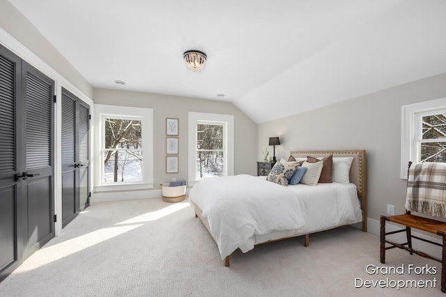 carpeted bedroom with lofted ceiling and two closets