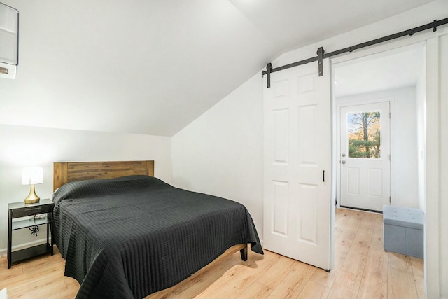 bedroom featuring lofted ceiling, a barn door, and light hardwood / wood-style flooring