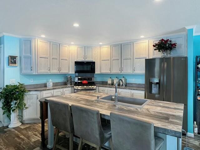 kitchen with appliances with stainless steel finishes, sink, ornamental molding, dark hardwood / wood-style flooring, and a breakfast bar