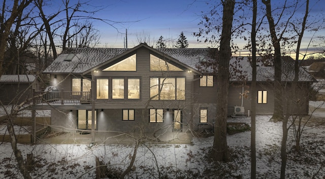 back of house at dusk featuring a deck and roof with shingles