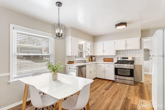 kitchen featuring stainless steel appliances, plenty of natural light, white cabinets, and decorative light fixtures