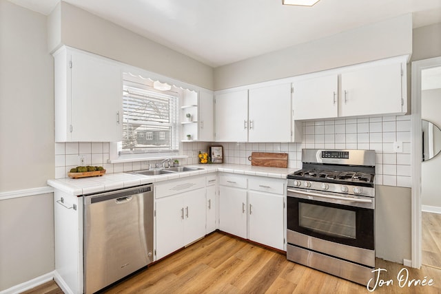 kitchen with sink, white cabinetry, light hardwood / wood-style flooring, appliances with stainless steel finishes, and tile counters