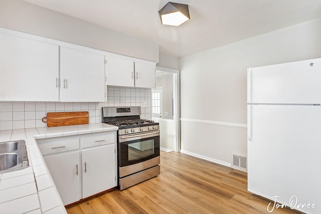 kitchen featuring white cabinets, backsplash, white fridge, tile counters, and gas range