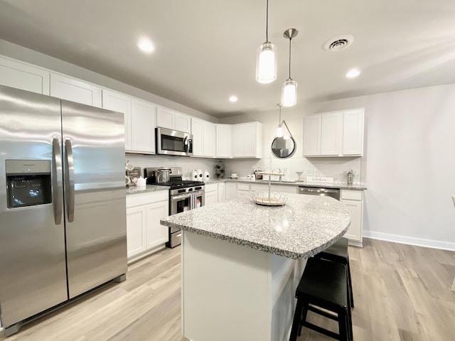 kitchen featuring appliances with stainless steel finishes, hanging light fixtures, a center island, light stone counters, and white cabinets