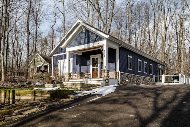 view of front of home featuring stone siding, aphalt driveway, and a porch